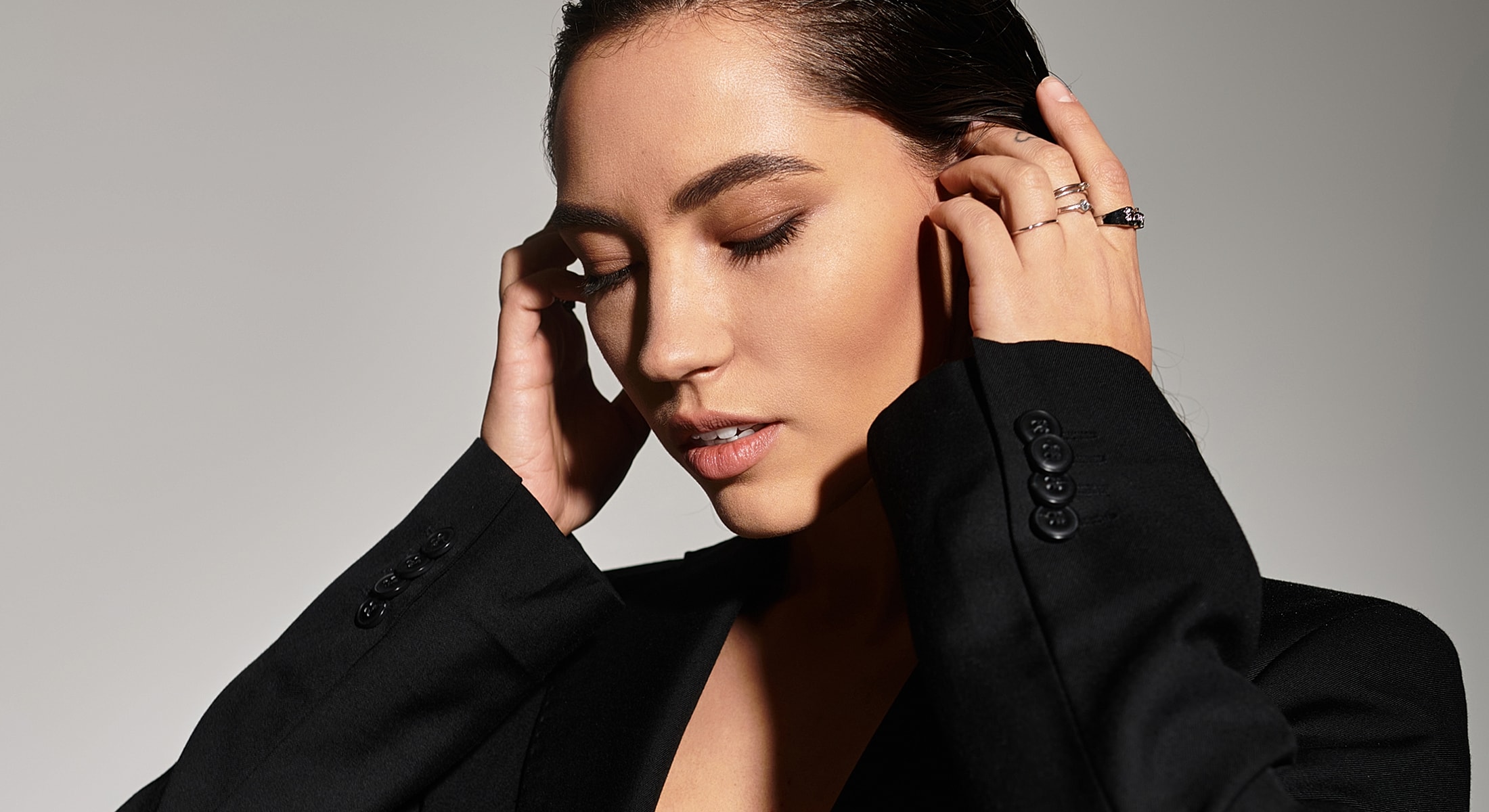 Woman in black suit with hands on head.